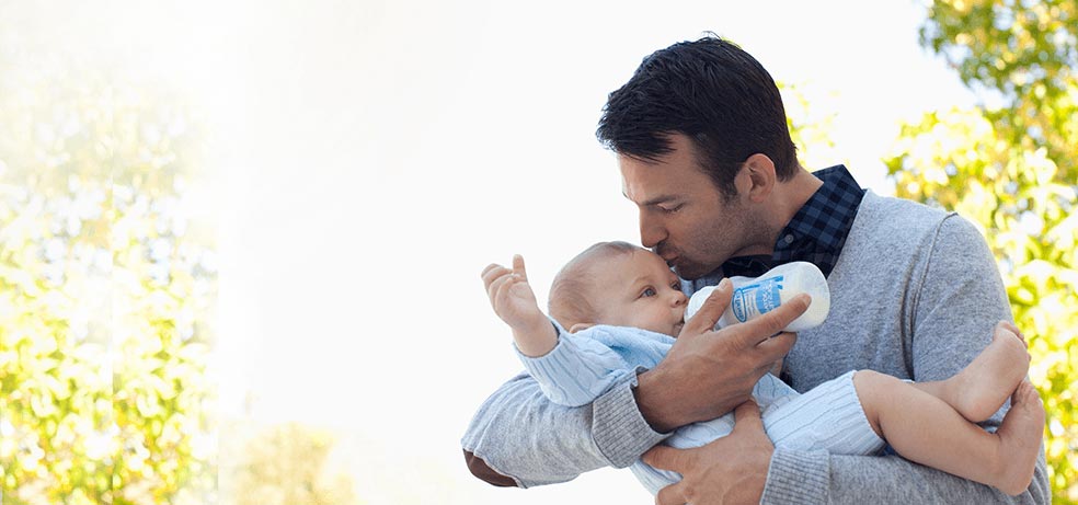 A father kissing his baby boy on the forehead while also feeding him with a bottle of formula