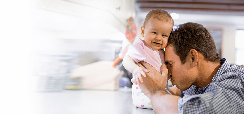 A father blowing on a baby's belly near the kitchen counter