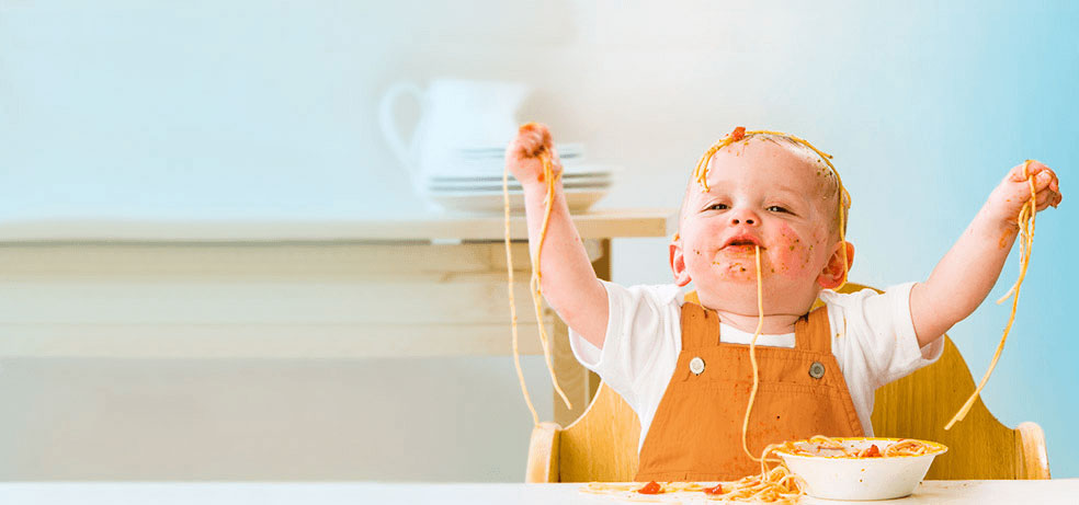 Toddler kid playing with his food and throwing spaghetti all over himself