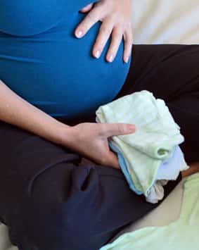 אישה בהריון יושבת על המיטה ואורזת תיק לחדר לידה