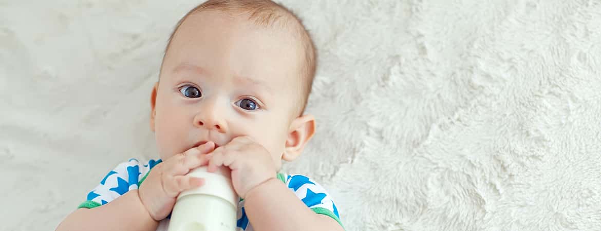 תינוק שוכב על שמיכה ושותה בקבוק חלב