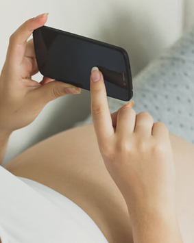 אישה בהריון שוכבת על הספה ומסתכלת בטלפון הסלולארי