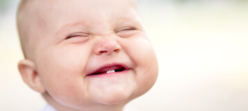 תינוק מחייך עם שתי שיניים תחתונות בפה