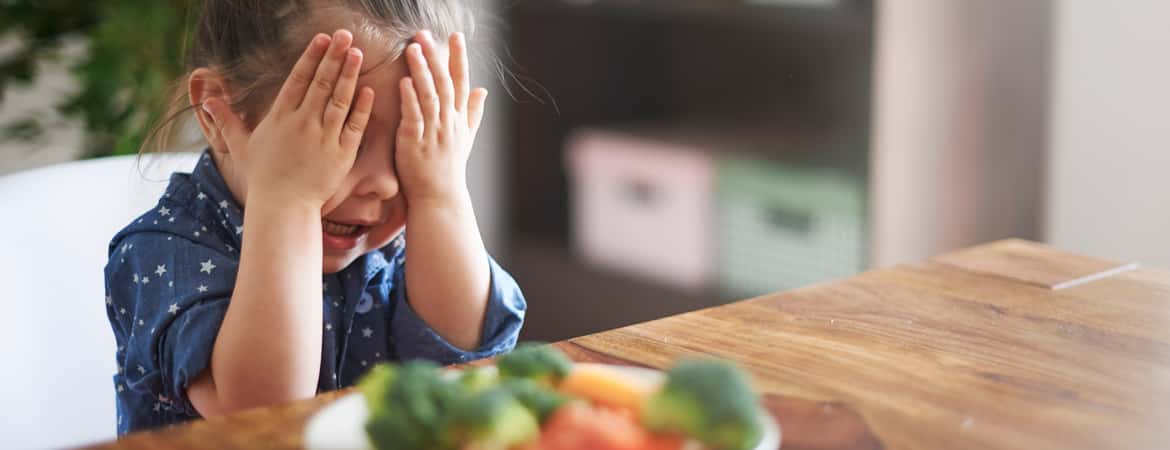 ילדה מכסה את עינייה מול צלחת ירקות