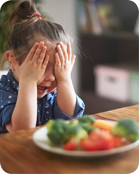 ילדה מכסה את עינייה מול צלחת ירקות