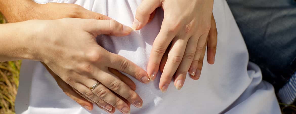 ידיים של גבר ואישה יוצרים לב על בטן של אישה הרה