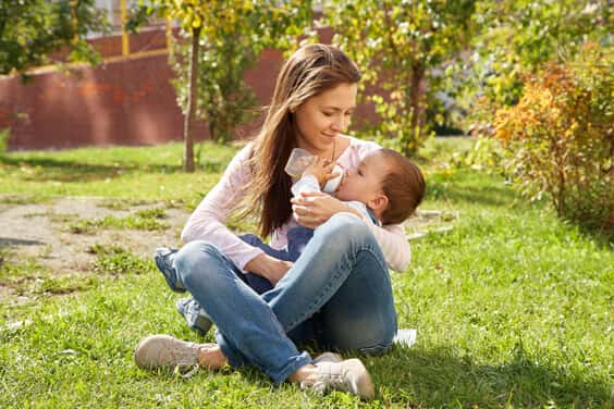 תינוק יושב על אמא בפארק ושותה בקבוק