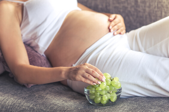 אישה בהריון שוכבת על הספה ואוכלת ענבים
