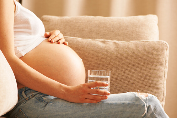 אישה בהריון יושבת על הספה ומחזיקה כוס
