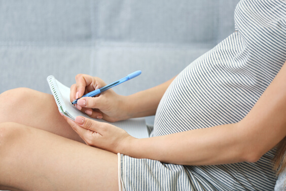 אישה בהריון יושבת על השטיח עם רשימה